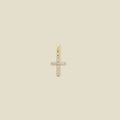 A small gold cross charm covered in small clear stones, set against a solid beige background.