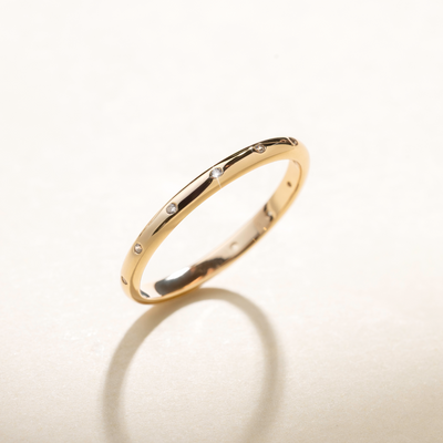 A polished gold ring with small clear accent stones inlayed around the exterior, set against a beige background with natural shadows.