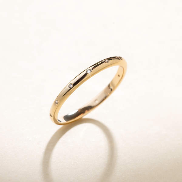 A polished gold ring with small clear accent stones inlayed around the exterior, set against a beige background with natural shadows.