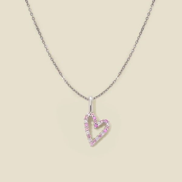 A dainty silver chain necklace with a silver heart charm with different pink colored stones, set against a solid beige background.