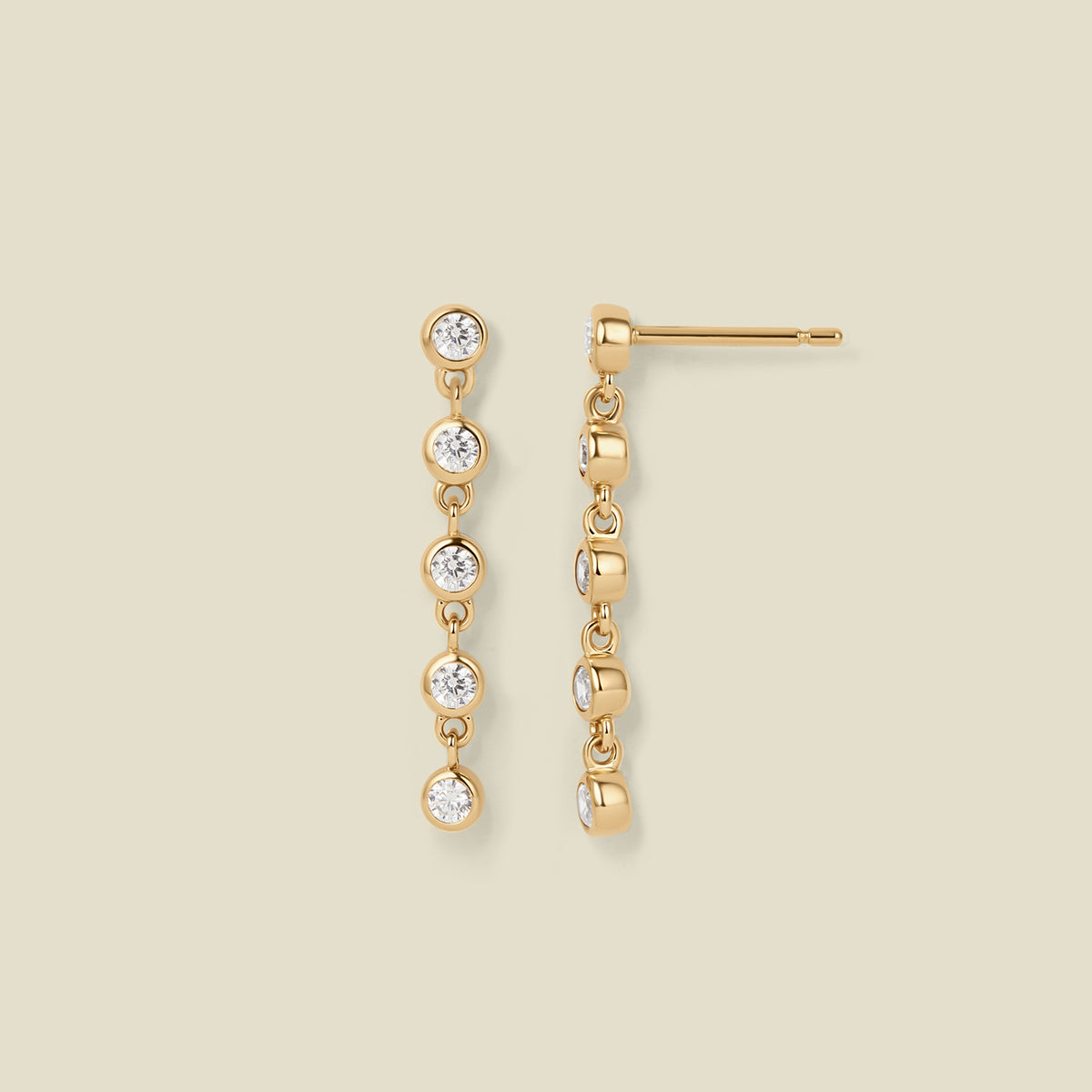A pair of gold stud earrings with five, round clear gemstones hanging vertically, set against a solid beige background.