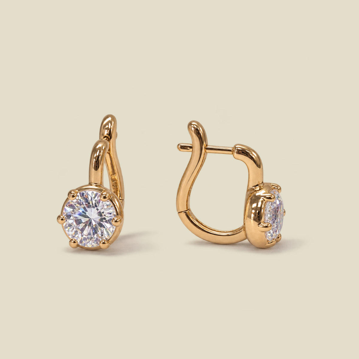 A pair of gold huggie hoop earrings with round-cut clear gemstones, shown from two angles on a solid light beige background.