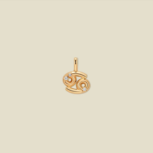 A gold pendant shaped like the Cancer zodiac symbol, featuring three small clear gemstones, centered on a solid light beige background.