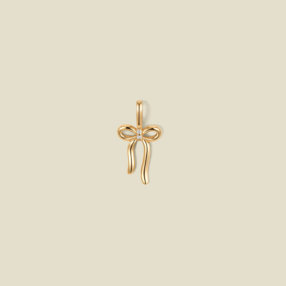 A gold bow shaped pendant charm with a small clear stone in the center.