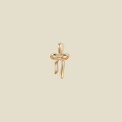 A gold bow shaped pendant charm with a small clear stone in the center.