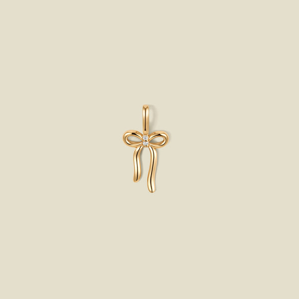 A gold bow shaped pendant charm with a small clear stone in the center.