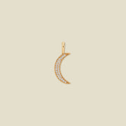 A gold crescent moon pendant adorned with small clear stones, centered on a solid beige background.