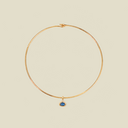 A delicate gold wire hoop necklace with a small oval blue gemstone pendant, displayed on a solid light beige background.