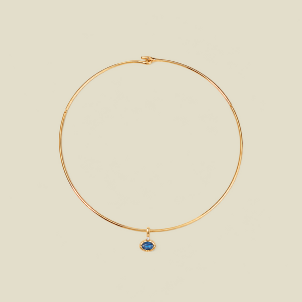 A delicate gold wire hoop necklace with a small oval blue gemstone pendant, displayed on a solid light beige background.