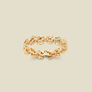 A gold floral-etched ring band with holly flowers and small clear gemstones, shown on a plain warm beige background. 