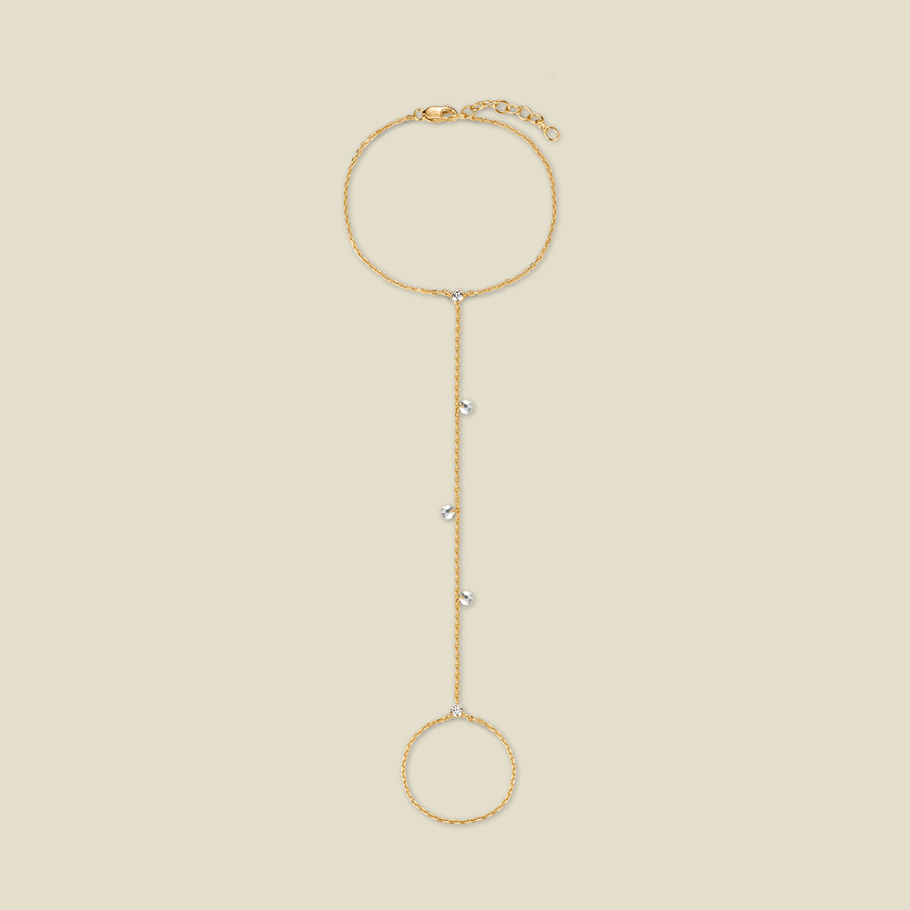 A dainty gold hand chain featuring small round clear crystals dangling throughout, shown against a solid beige background.
