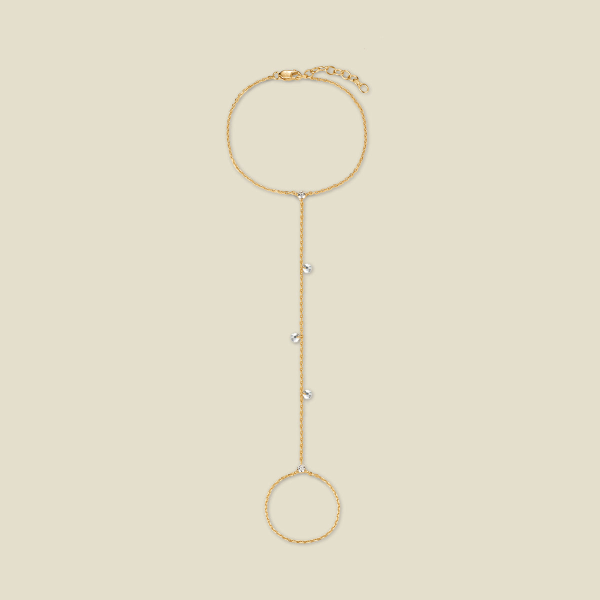 A dainty gold hand chain featuring small round clear crystals dangling throughout, shown against a solid beige background.