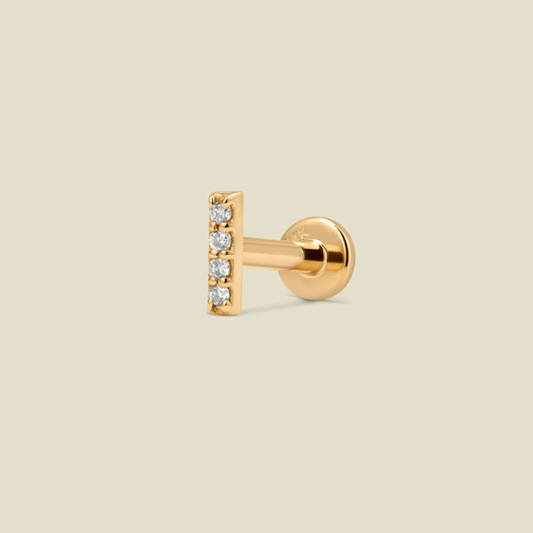 A gold bar shaped stud earring with four clear gemstones set vertically, shown from a side profile against a solid light beige background.