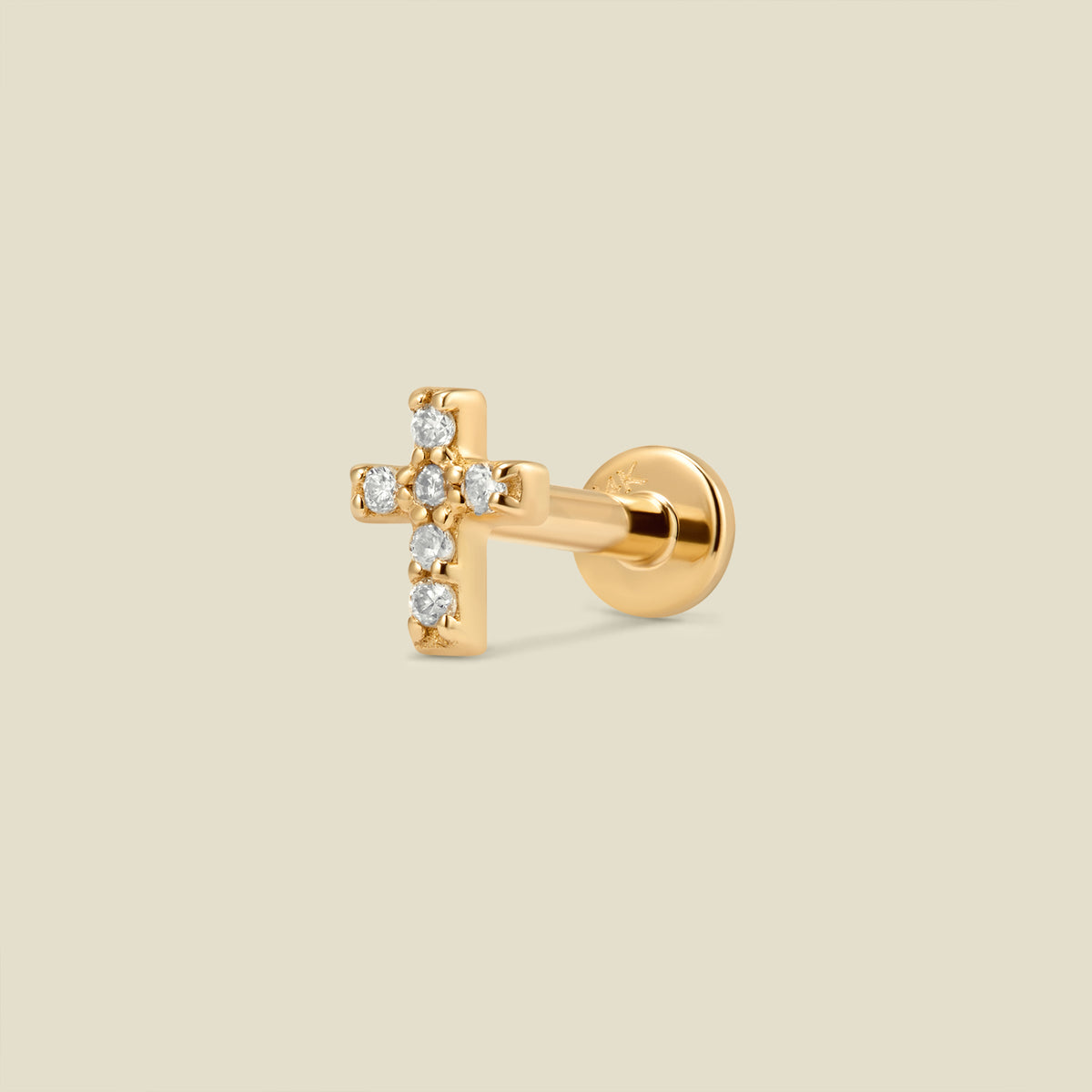 A gold cross stud earring with clear diamonds and a flat earring back, set against a light beige background.
