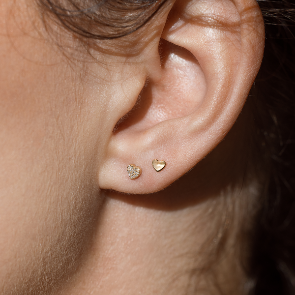 Close up of an ear wearing two heart shaped gold stud earrings, one with diamonds.