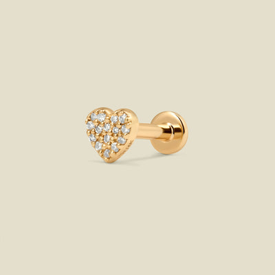A gold heart-shaped stud earring with pave diamonds and a flat earring back, set against a light beige background.