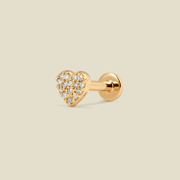 A gold heart-shaped stud earring with pave diamonds and a flat earring back, set against a light beige background.