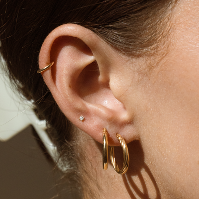 Close-up of an ear wearing three gold hoop earrings, and a small prong-set diamond stud with a neutral background