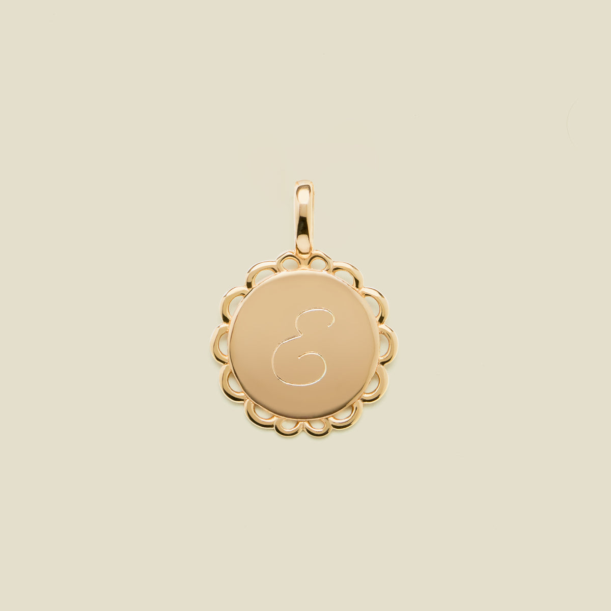 Gold pendant with engraved letter 'E' on a beige background