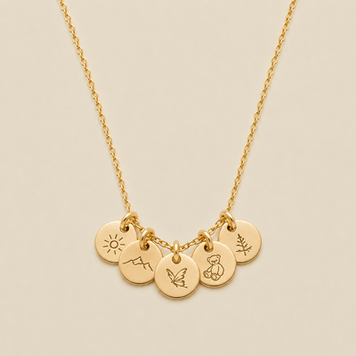 A gold chain necklace with five small round engraved charms featuring minimalist symbols of a sun, a mountain, butterfly, teddy bear, and pine tree, displayed on a light beige background.