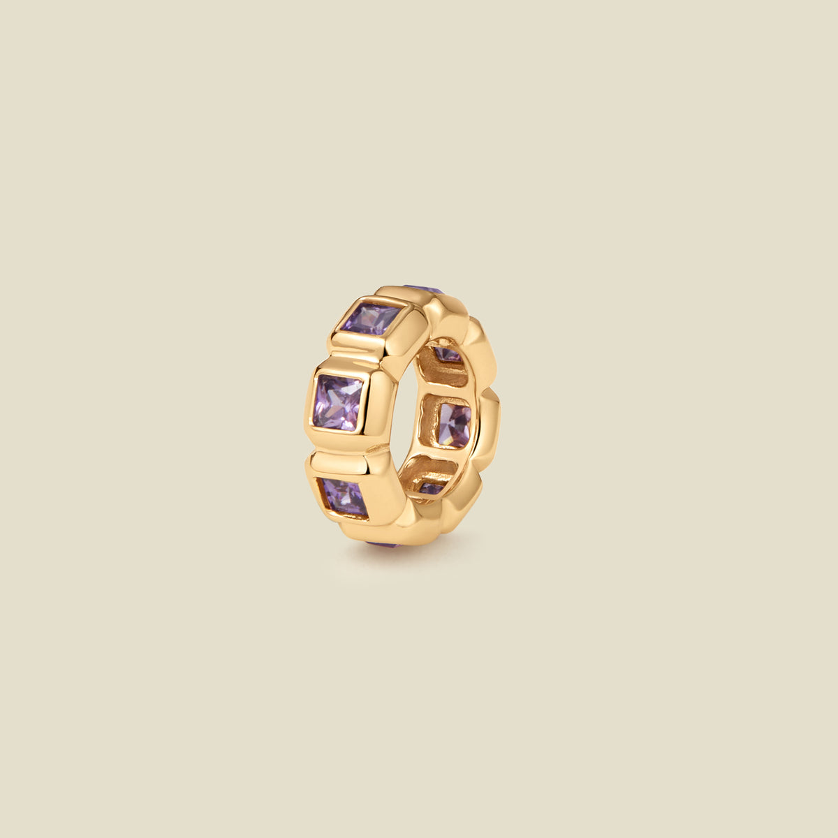 A gold ring charm with multiple bezel set square-cut purple gemstones set side by side to create the band, shown on a solid beige background.