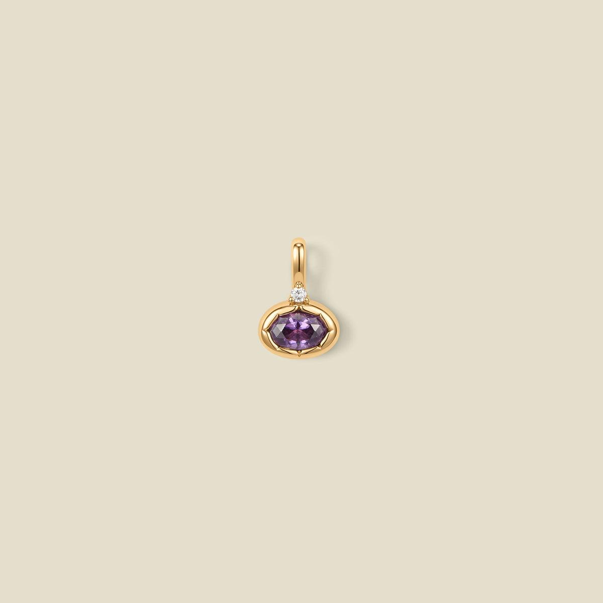 A gold oval pendant charm with a purple bezel-set oval gemstone and a clear accent stone on top, set against a solid beige background.
