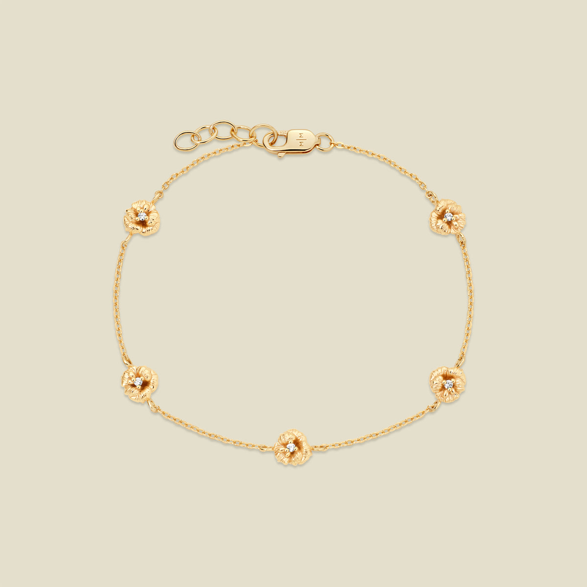 A delicate gold chain bracelet featuring five ornate, textured gold violet charms with small clear stones, arranged in a circle on a light beige background.