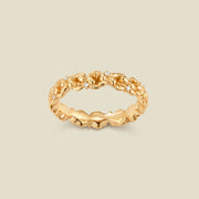 A gold floral-etched ring band with textured violet flowers and small clear gemstones, shown on a plain warm beige background. 