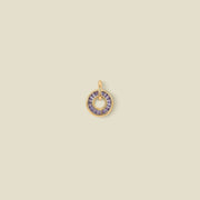 A circular gold pendant featuring purple baguette-cut stones around a hollow center, displayed against a solid light beige background.