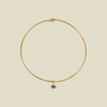 A thin gold wire necklace with a small purple oval gemstone charm, displayed on a solid beige background.