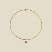 A thin gold wire necklace with a small purple oval gemstone charm, displayed on a solid beige background.