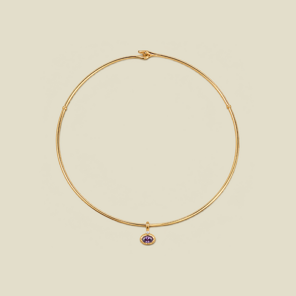 A thin gold wire necklace with a small purple oval gemstone charm, displayed on a solid beige background.