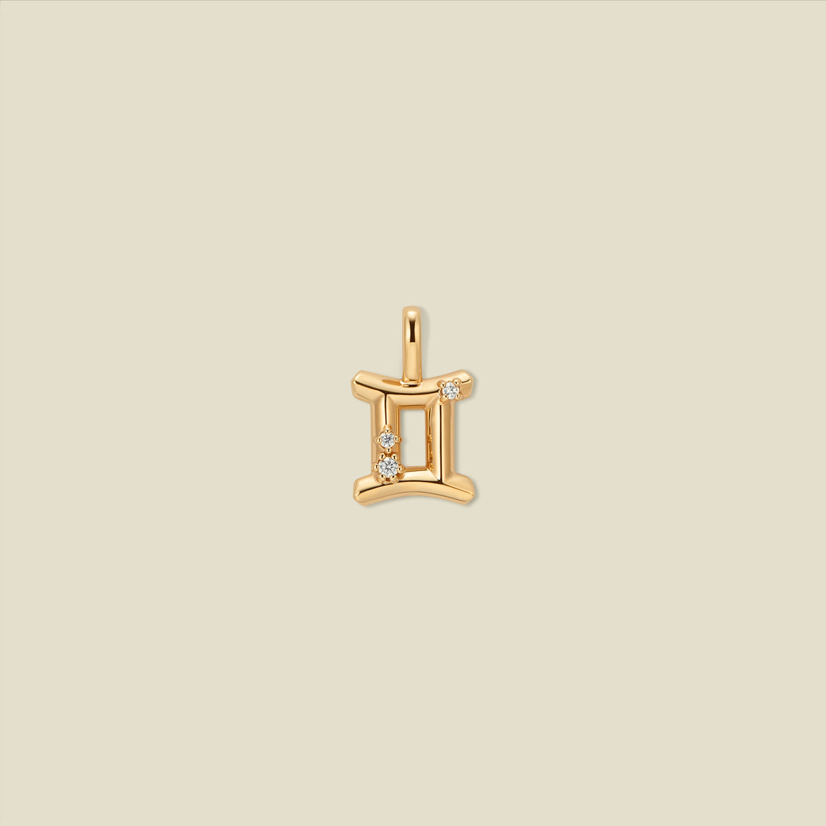 A gold pendant shaped like the Gemini zodiac symbol, featuring three small clear gemstones, centered on a solid light beige background.