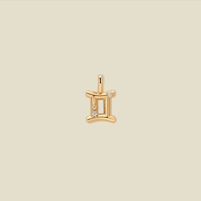 A gold pendant shaped like the Gemini zodiac symbol, featuring three small clear gemstones, centered on a solid light beige background.