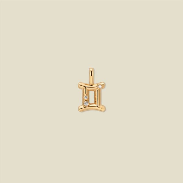 A gold pendant shaped like the Gemini zodiac symbol, featuring three small clear gemstones, centered on a solid light beige background.