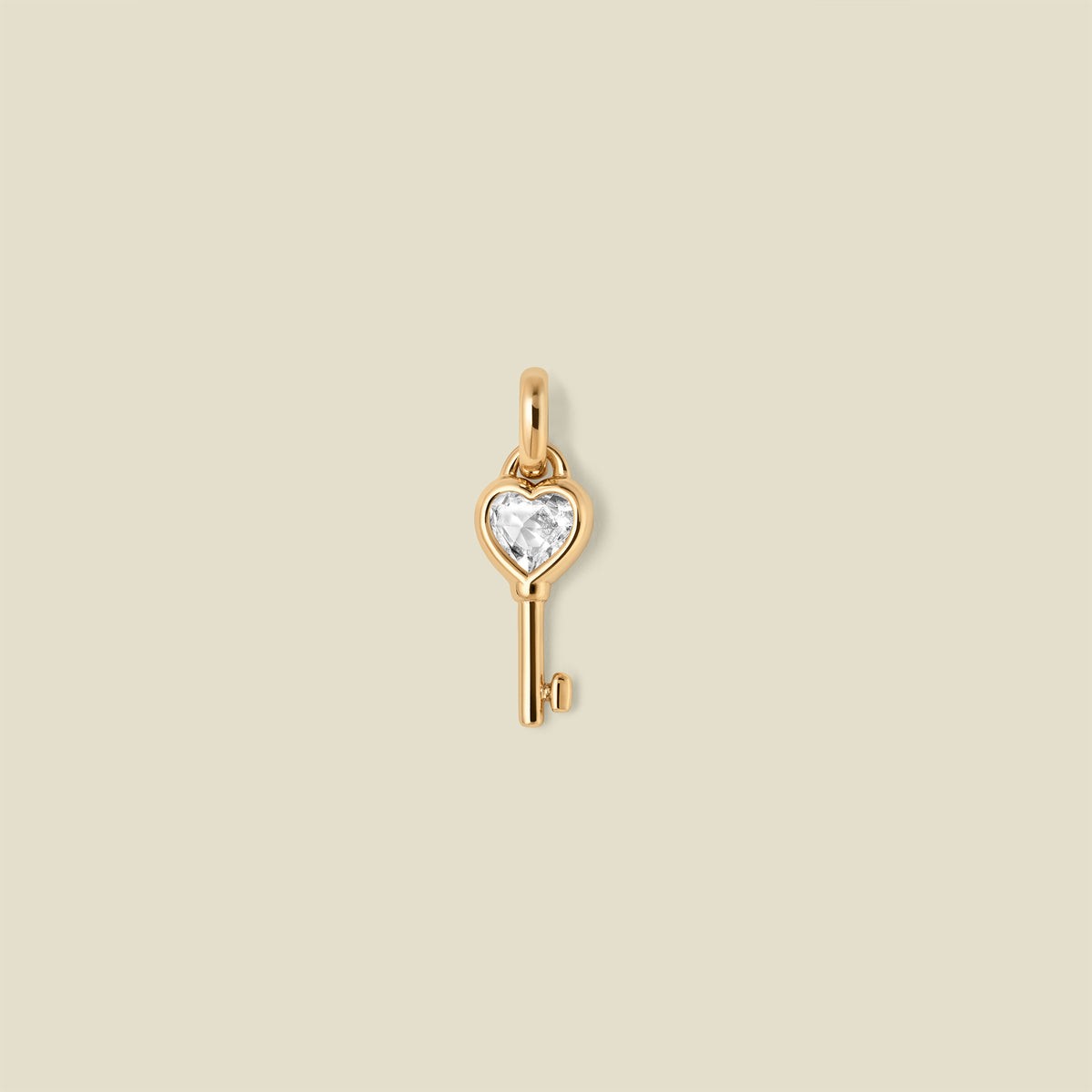 Gold key-shaped pendant with a heart shaped clear gemstone on a beige background