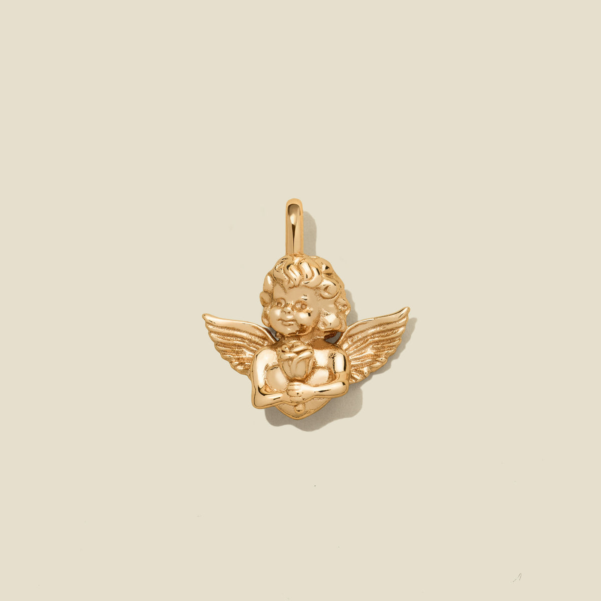 A small gold cherub pendant with wings and a bail at the top, centered on a warm beige background.