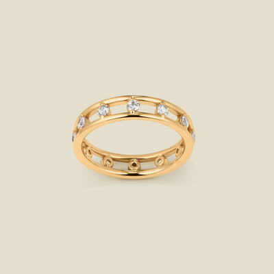 A yellow gold eternity-style band ring featuring a row of small clear marquise-cut stones set in open channels, shown on a plain warm beige background.
