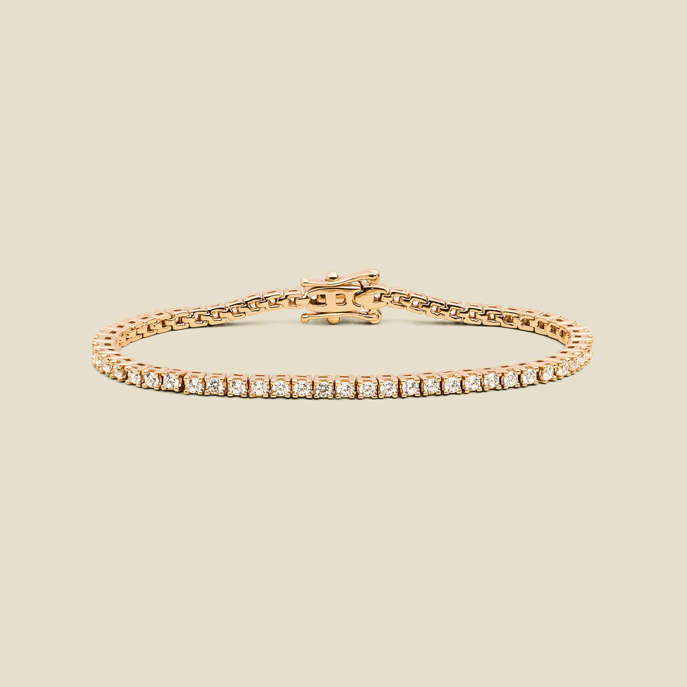 A gold tennis bracelet with clear square-cut gemstones, displayed on a solid light beige background.