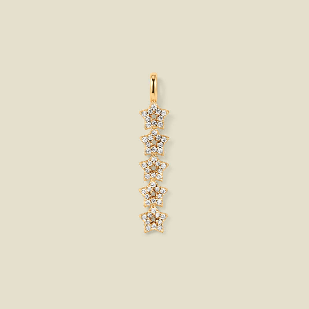 A gold pendant charm with five stars stacked vertically with clear stones, set against a solid beige background.