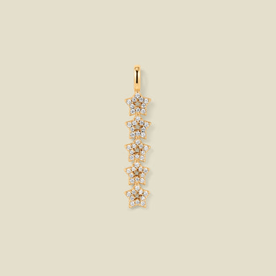 A gold pendant charm with five stars stacked vertically with clear stones, set against a solid beige background.