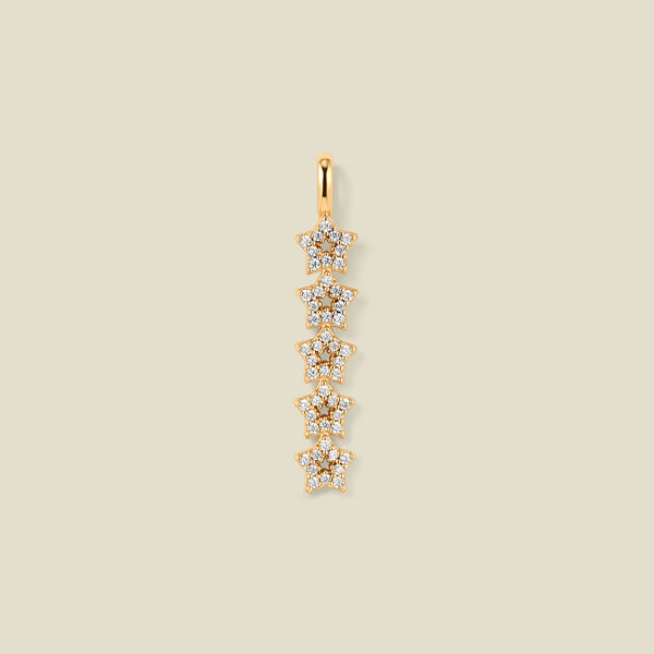 A gold pendant charm with five stars stacked vertically with clear stones, set against a solid beige background.