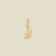 Gold initial "b" charm on a beige background