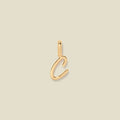 A polished gold initial pendant charm shaped like the letter 'C' in a cursive script, centered on a solid light beige background.