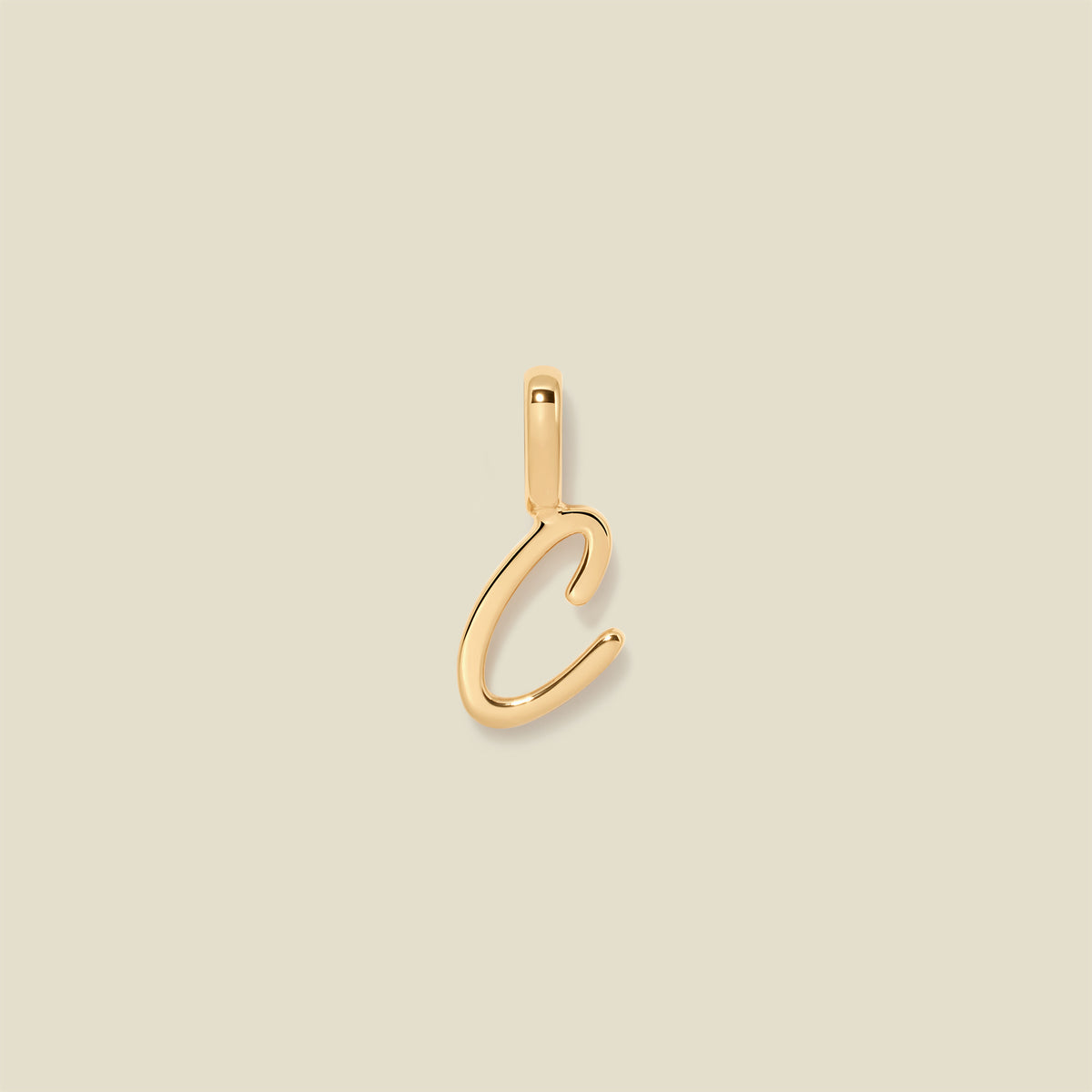 A polished gold initial pendant charm shaped like the letter 'C' in a cursive script, centered on a solid light beige background.