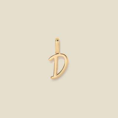 A polished gold initial pendant charm shaped like the letter 'D' in a cursive script, centered on a solid light beige background.