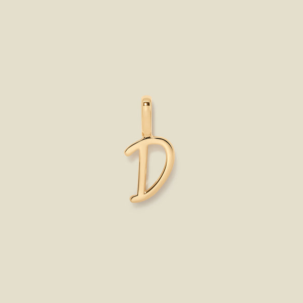 A polished gold initial pendant charm shaped like the letter 'D' in a cursive script, centered on a solid light beige background.