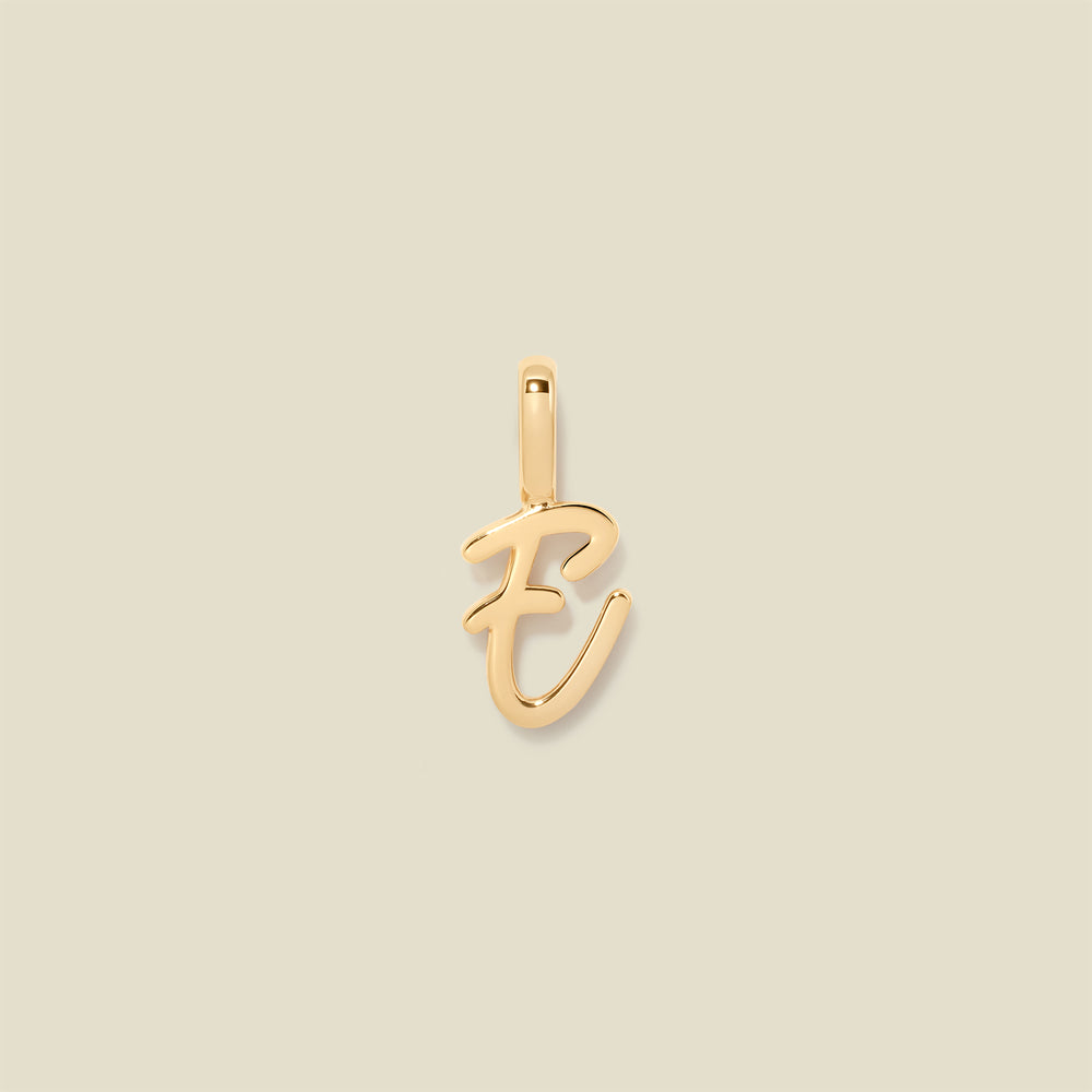 A polished gold initial pendant charm shaped like the letter 'E' in a cursive script, centered on a solid light beige background.