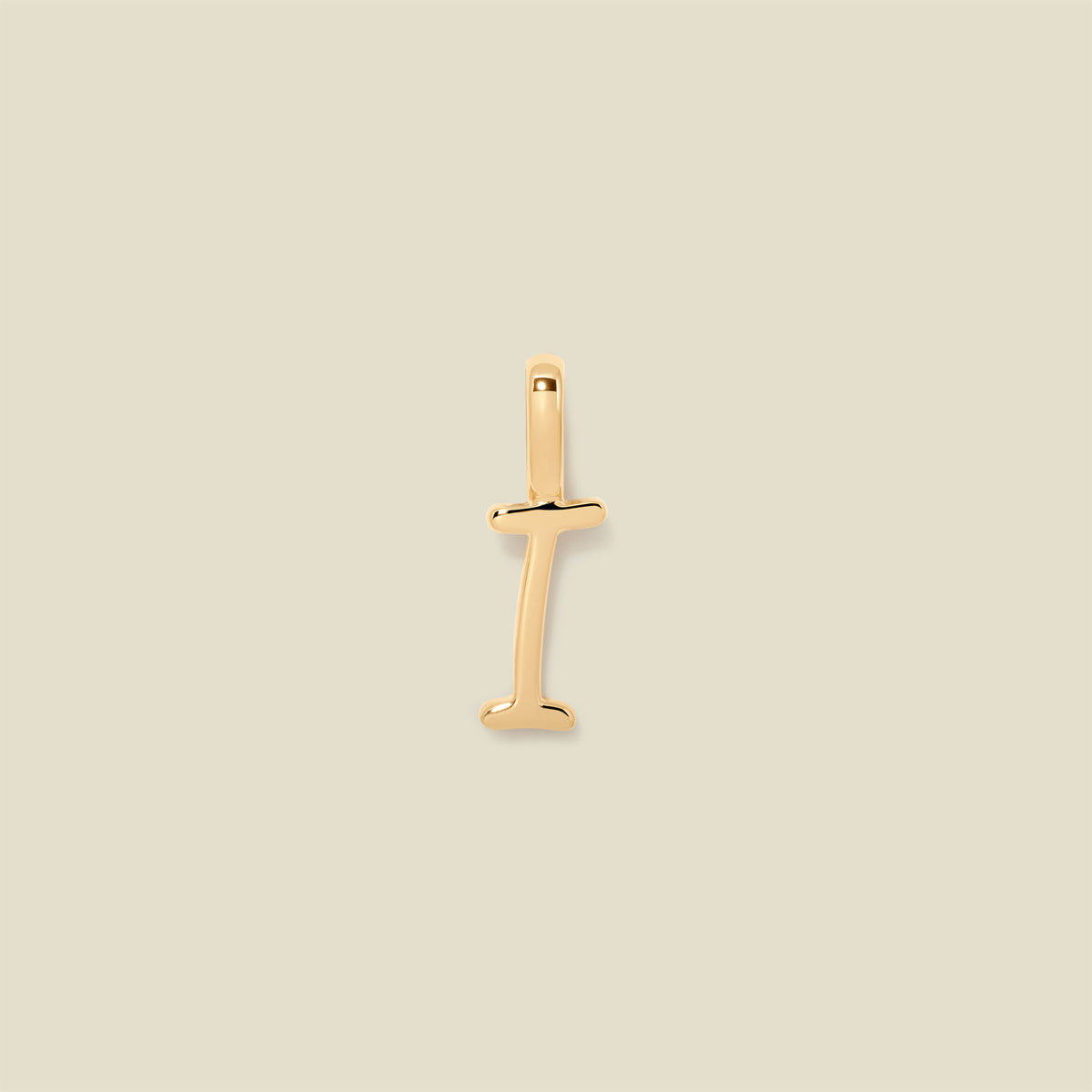 A polished gold initial pendant charm shaped like the letter 'I' in a cursive script, centered on a solid light beige background.