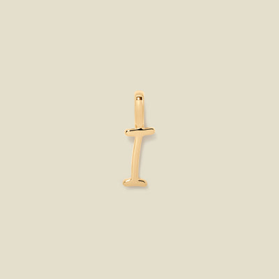 A polished gold initial pendant charm shaped like the letter 'I' in a cursive script, centered on a solid light beige background.